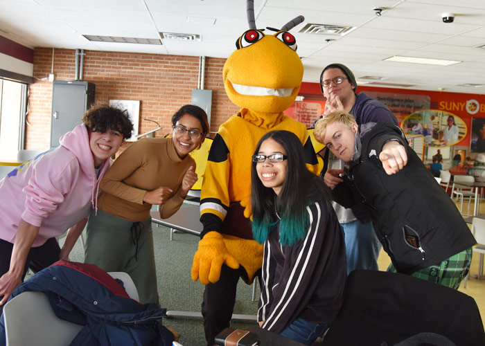 A group of Students crowd around Stinger, the college Hornet mascot, and give thumbs-up signs